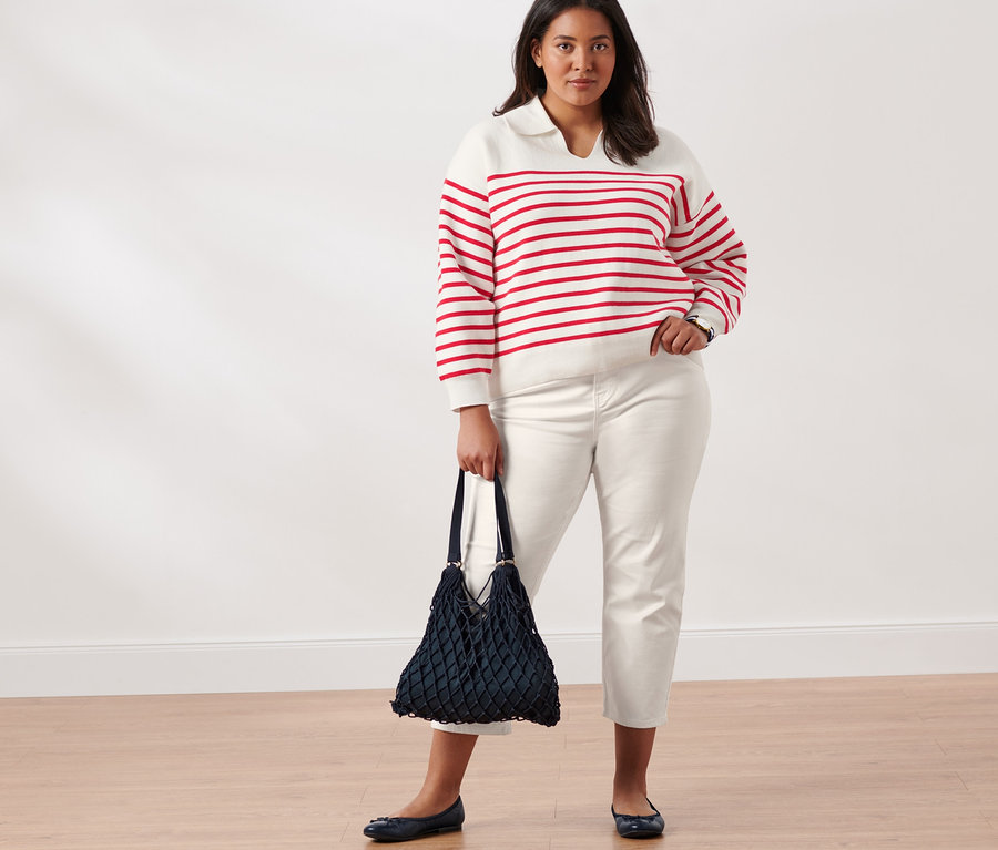 Frau posiert in weiß-rotem Strickpullover mit Kragen, Slimfit-Jeans, Leder-Ballerinas, mit Netztasche und Quarz-Armbanduhr aus Edelstahl.