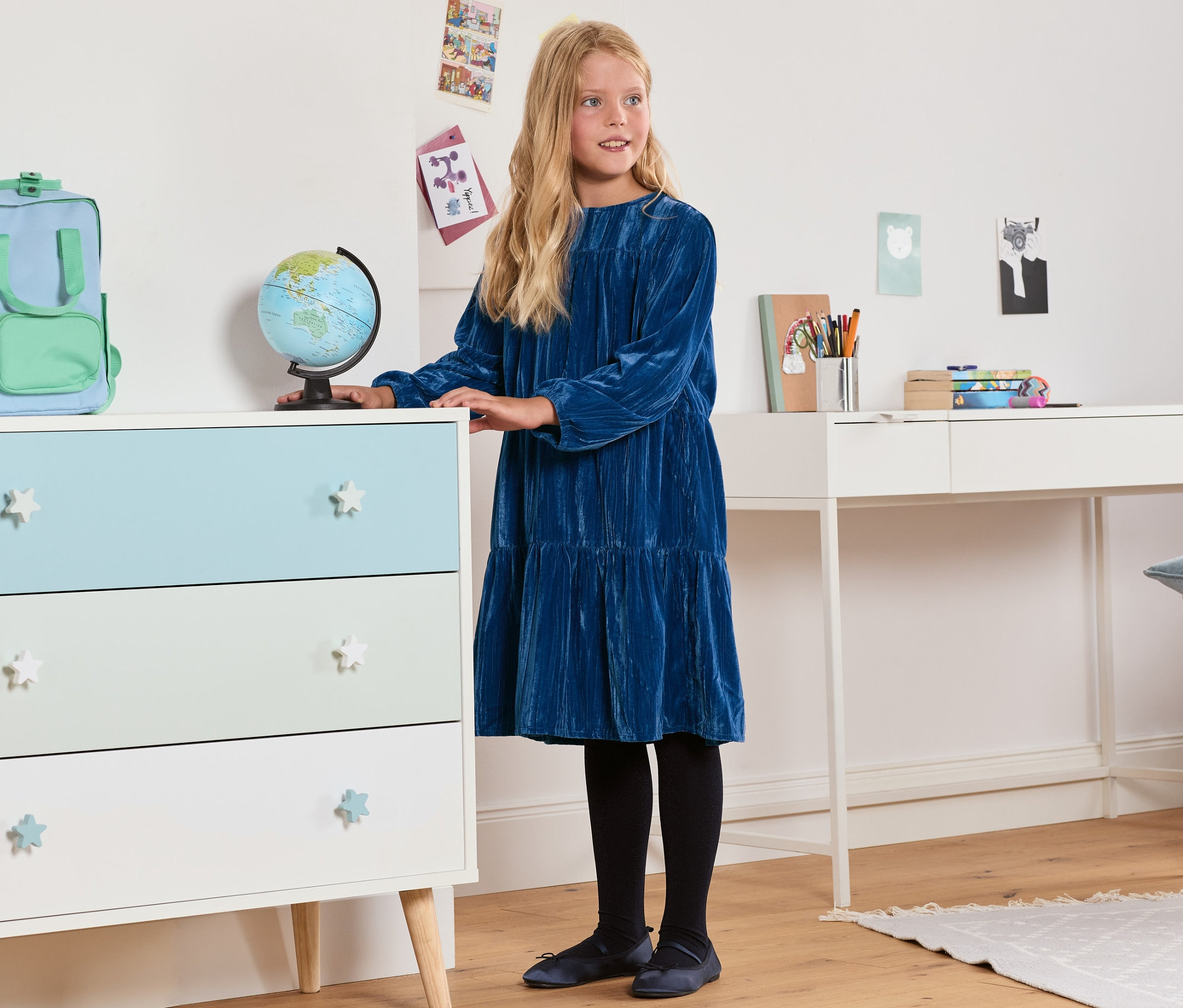 Mädchen steht im Zimmer und trägt ein Samtkleid.