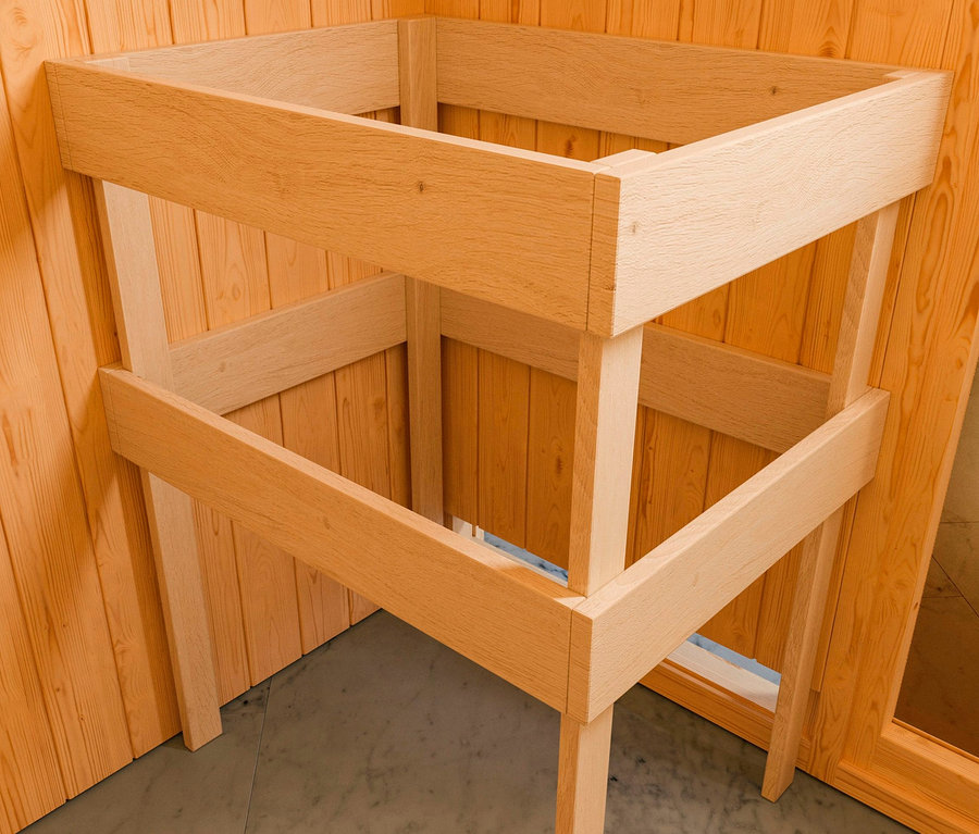 Unfertige naturfarbene Holzkonstruktion des Karibu Saunahauses »Linda Bio« steht in einer Ecke des Raumes mit Holzvertäfelung.