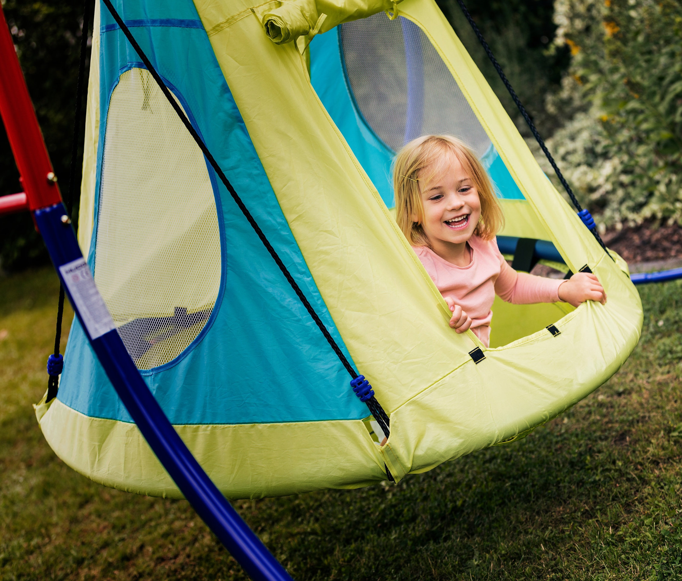 Ein Mädchen lacht in der HUDORA Nestschaukel-Zelt Cosy Castle 110.