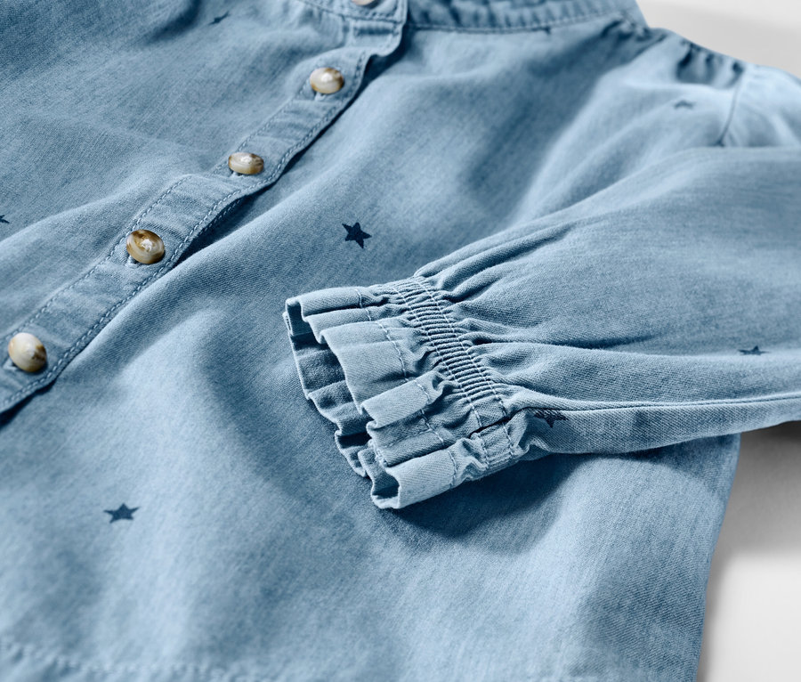 Detailaufnahme einer Kinder-Chambray-Bluse mit Sternen, Knöpfen und gerafften Ärmeln.