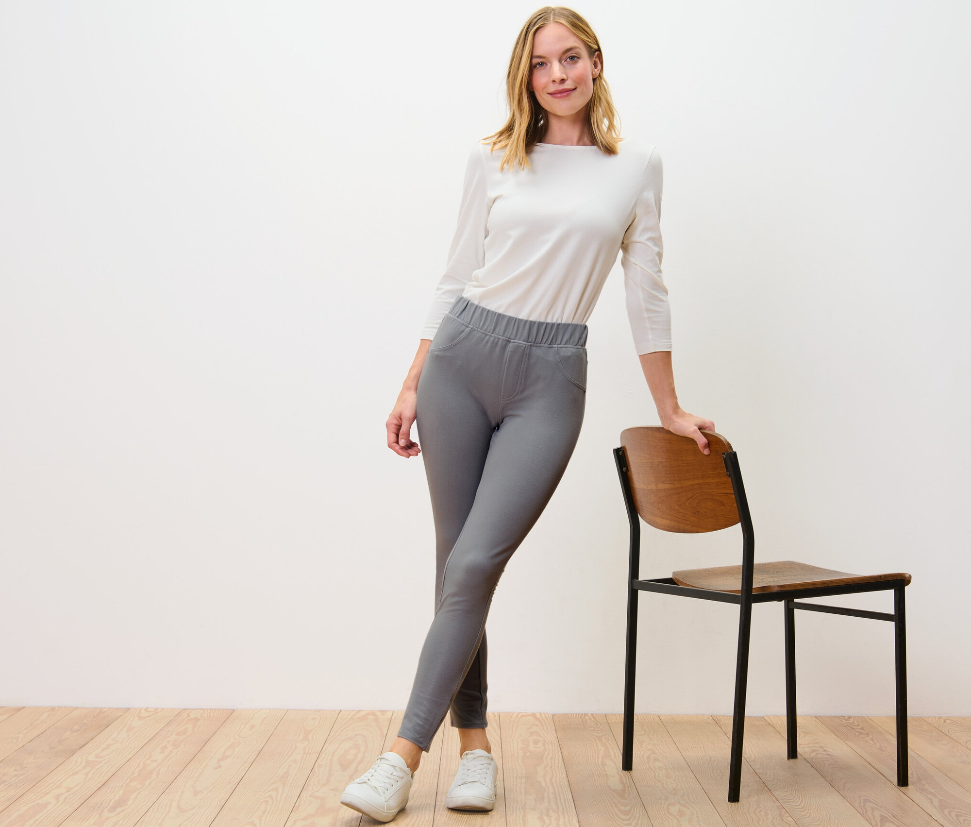 Frau posiert in grauen Leggings in Jeansoptik neben einem Stuhl.