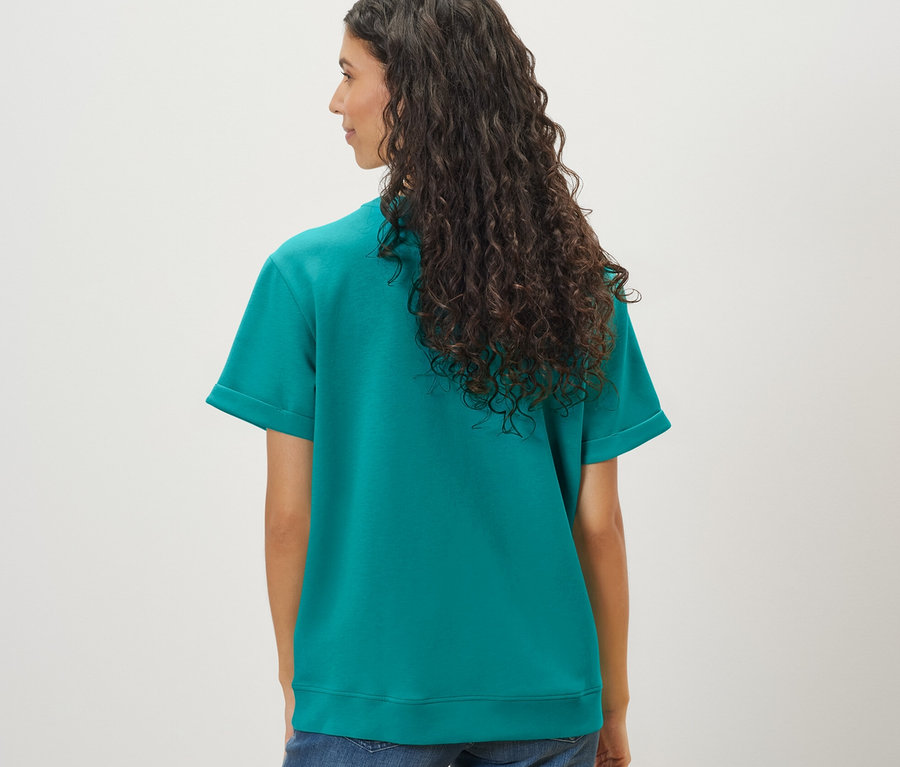 Frau mit langen gewellten Haaren trägt ein Shirt aus Modalmix in Aqua und Jeans.