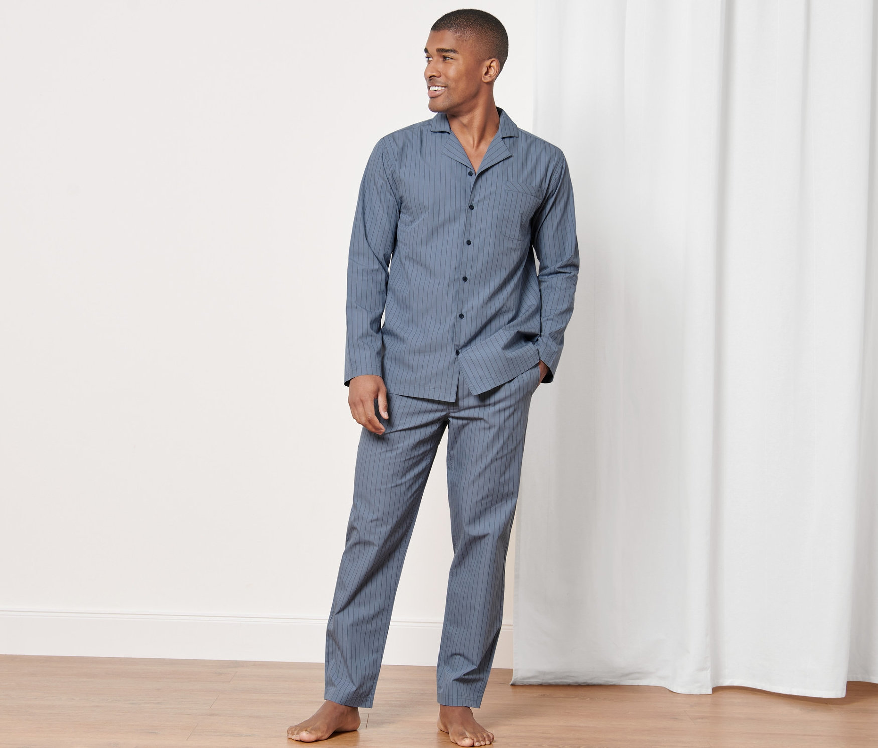 Mann posiert in einem gewebten Pyjama in einem Raum.