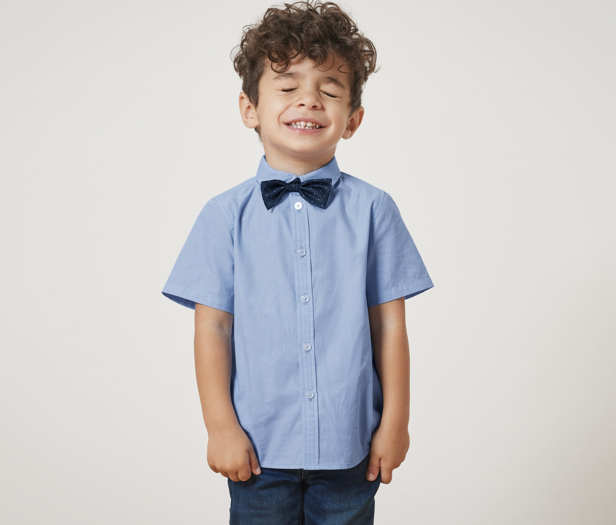 Junge mit geschlossenen Augen trägt ein Kinderhemd mit Fliege.