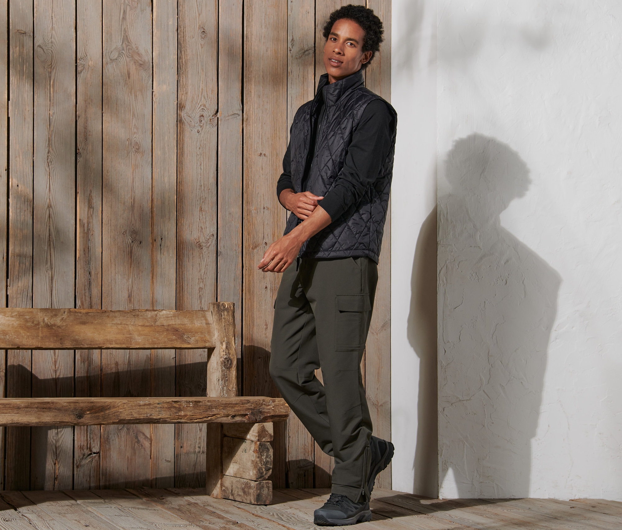 Mann steht und trägt eine Thermohose, eine Weste und Schuhe.