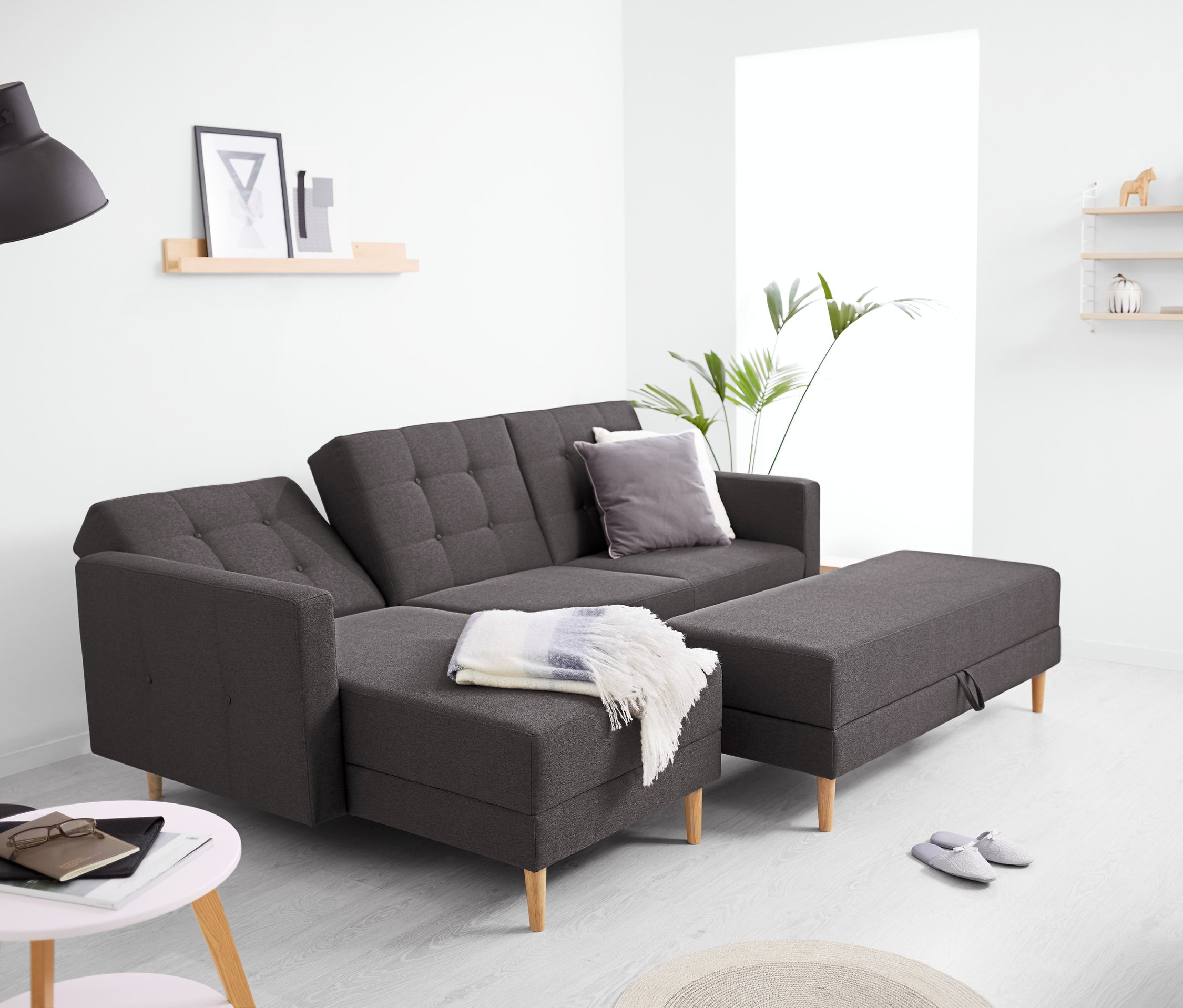 Ein Federkern-Eckschlafsofa mit Stauraumbank steht im Wohnzimmer. Im Hintergrund befinden sich eine Lampe und ein Regal.