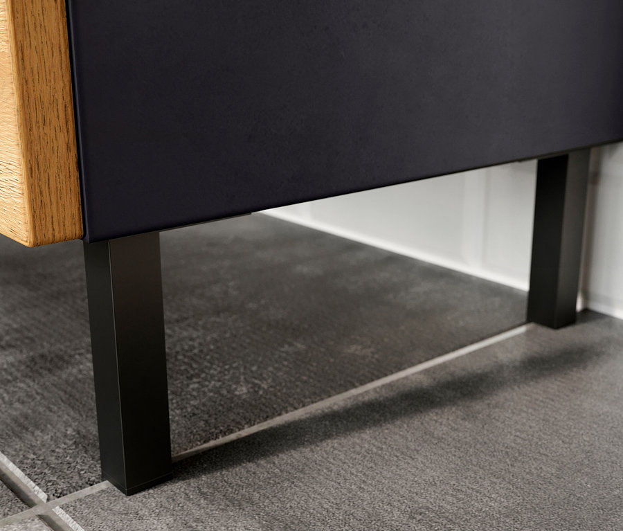 Detail eines »Salinas« Waschbeckenunterschranks, klein, graphit/eiche, mit schwarzen Füßen auf grauem Boden.