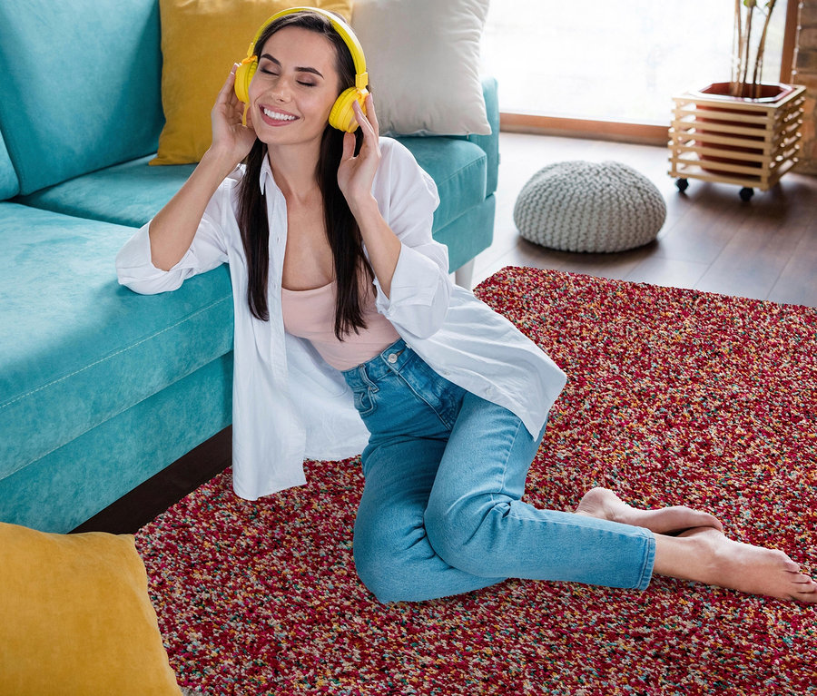 Frau sitzt auf Teppich »Relic«, autumn spice und hört Musik mit Kopfhörern.