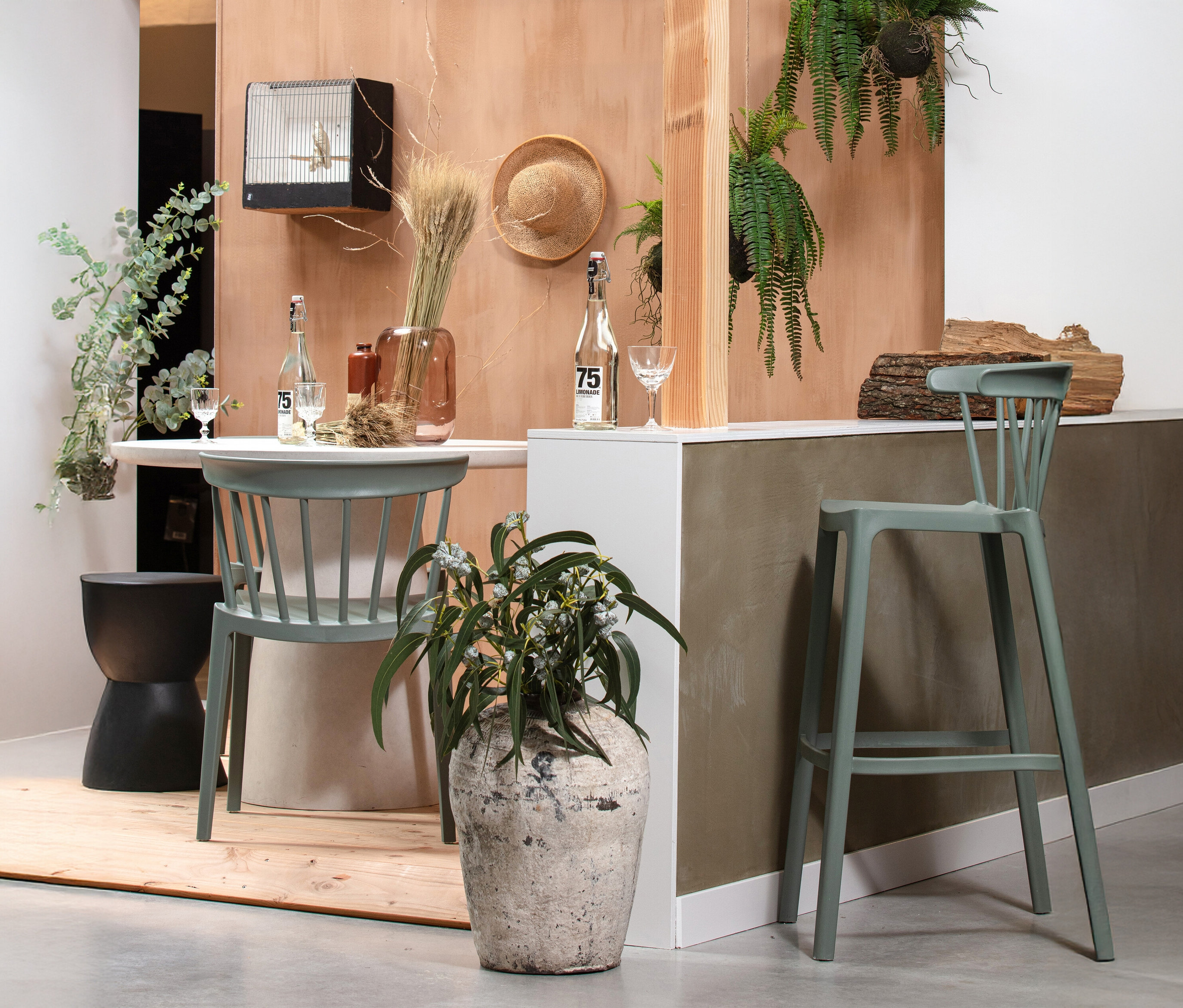Dekorativer Innenraum mit einem Tisch, Stühlen, Pflanzen und dekorativen Elementen wie einer Vogelscheuche und einer Flasche.
