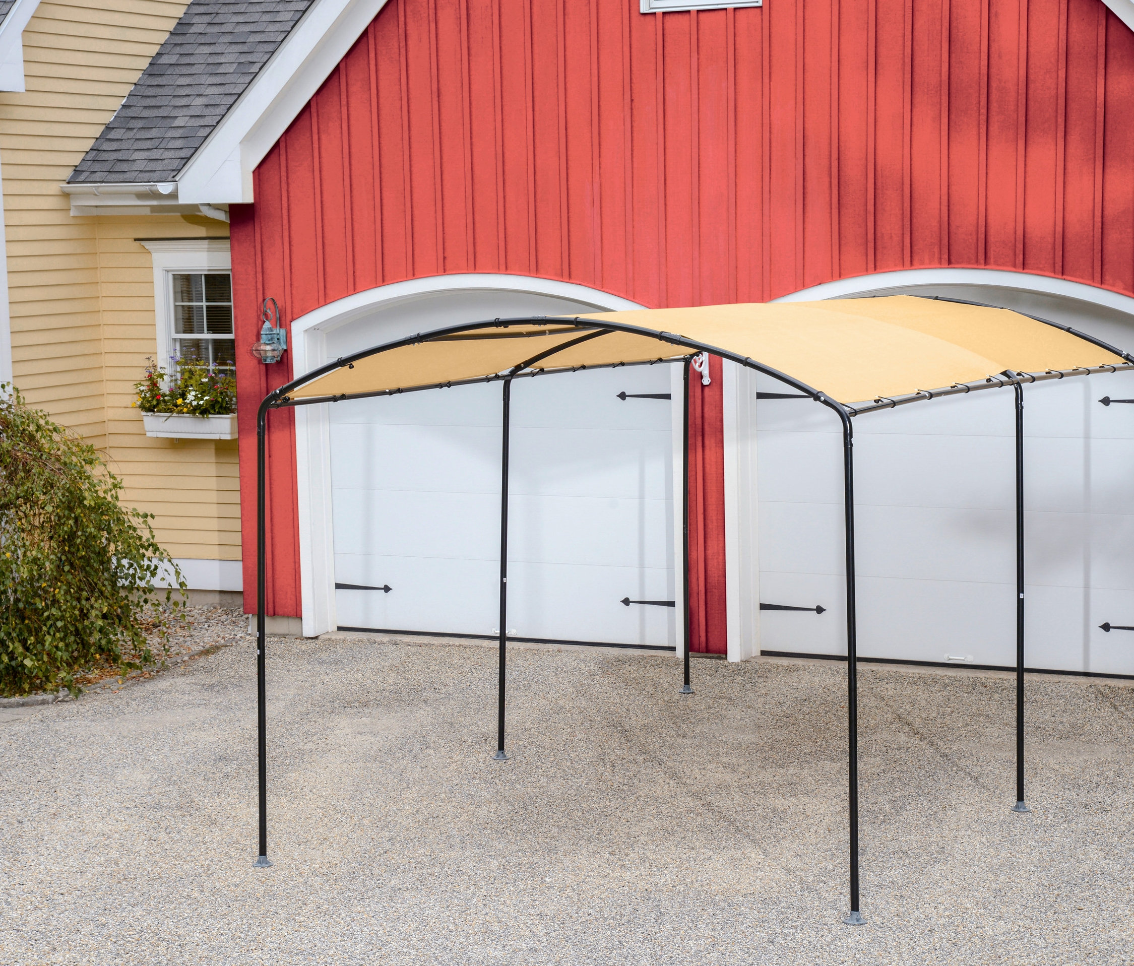 Schwarzes Runddach-Carport steht auf einer Schotterauffahrt vor einer roten Garage.