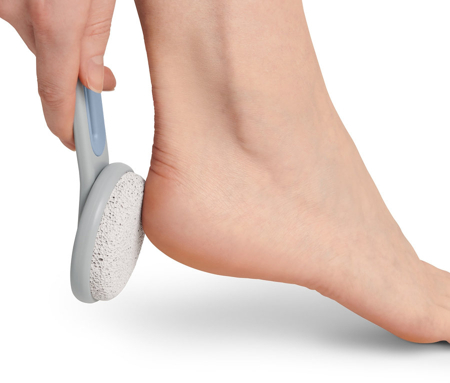 Eine Hand benutzt einen Bimsstein an der Ferse eines Fußes. Fußpflege-Set.