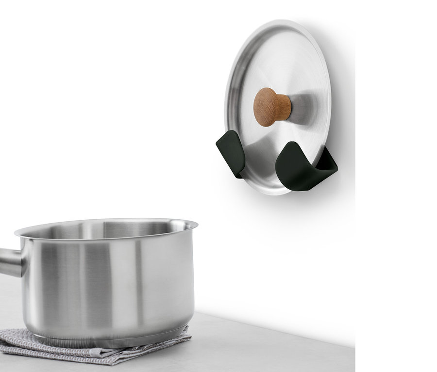 Ein Edelstahlkochtopf mit Holzgriff steht auf einem grauen Tuch. An der Wand sind 4 Wandhalterungen für Deckel.