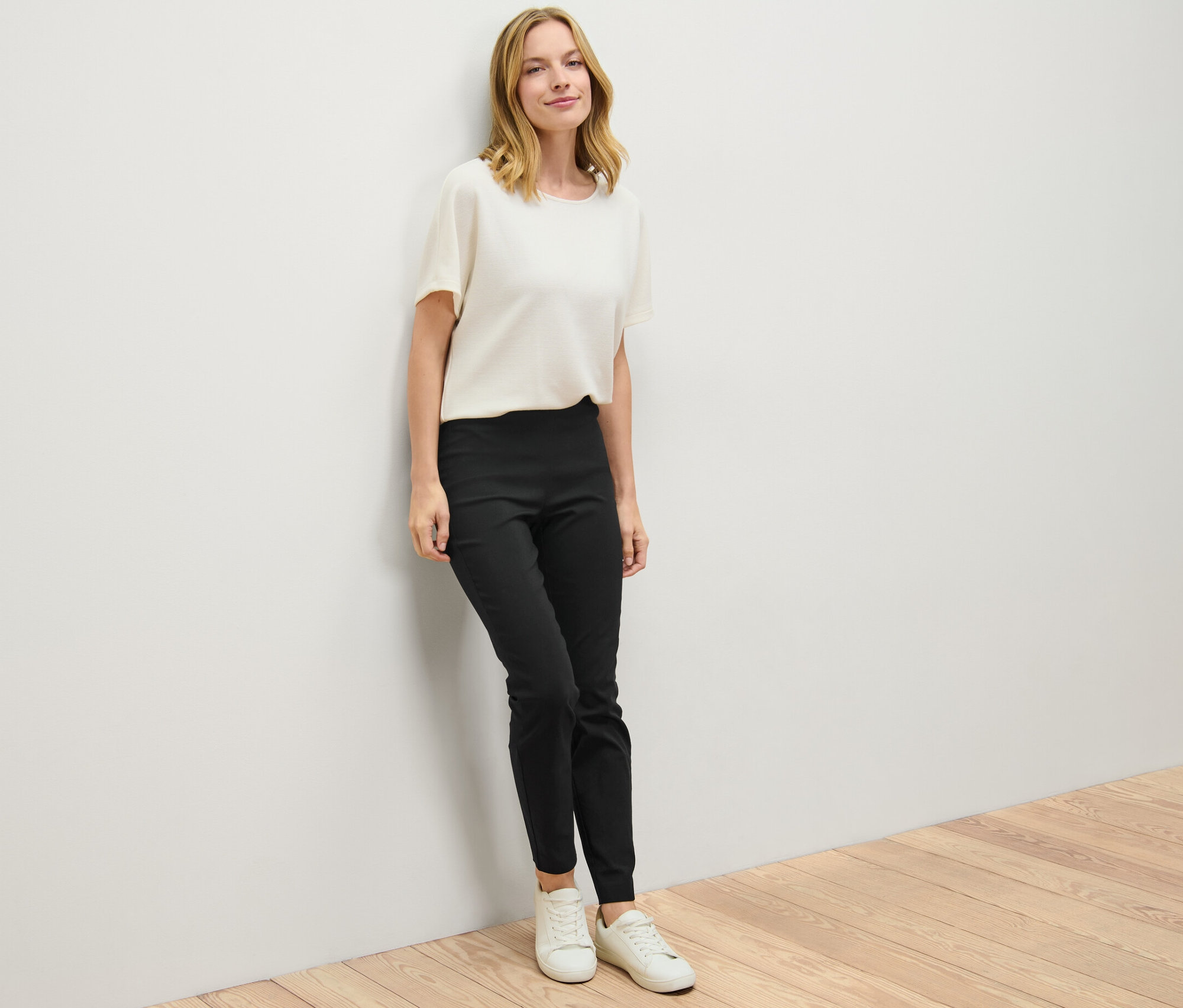 Eine Frau lehnt an einer Wand und trägt eine schwarze Stretchhose.