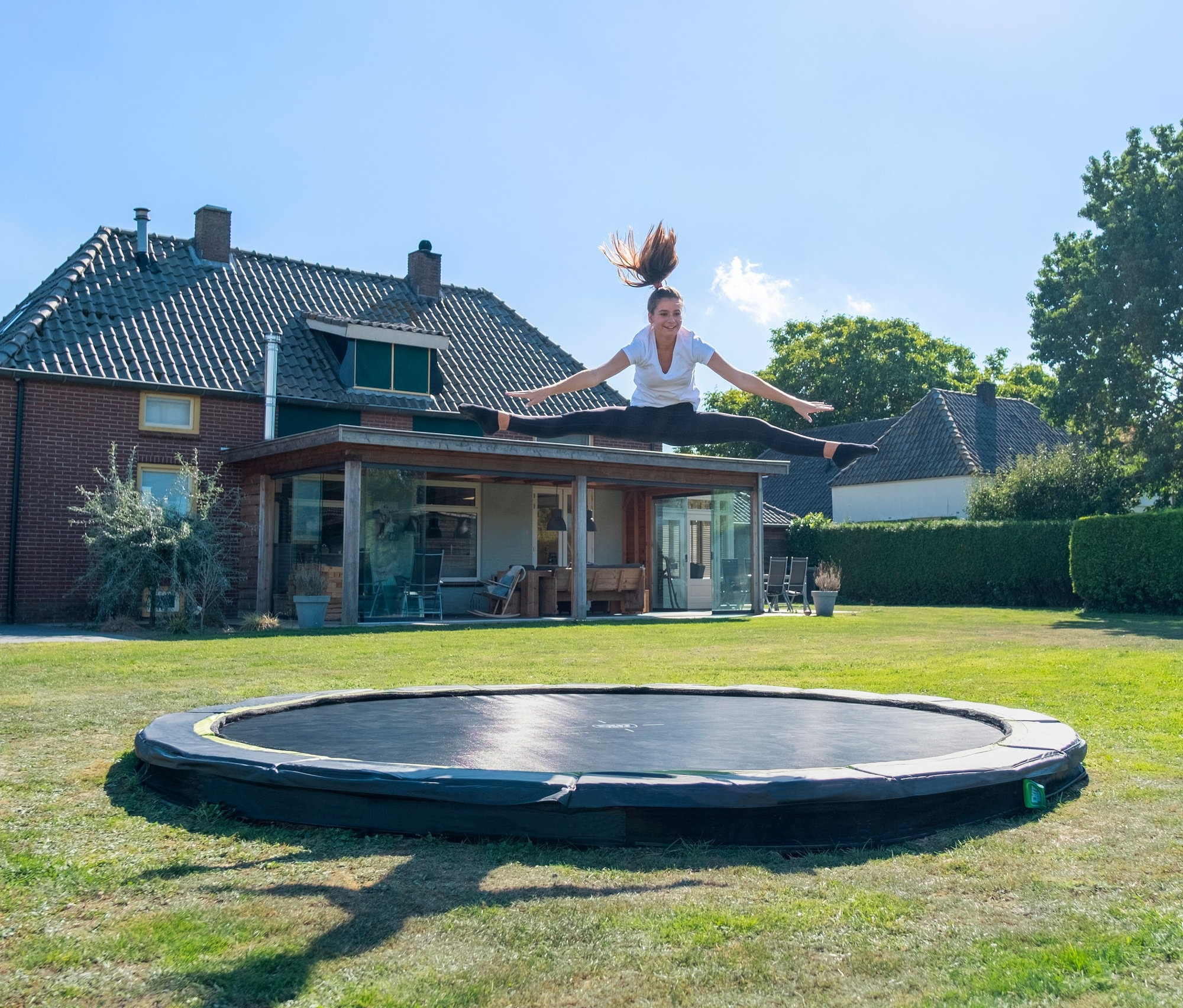 Eine junge Frau macht einen Spagat in der Luft über einem EXIT Bodentrampolin »Silhouette sports«, Ø ca. 366 cm.