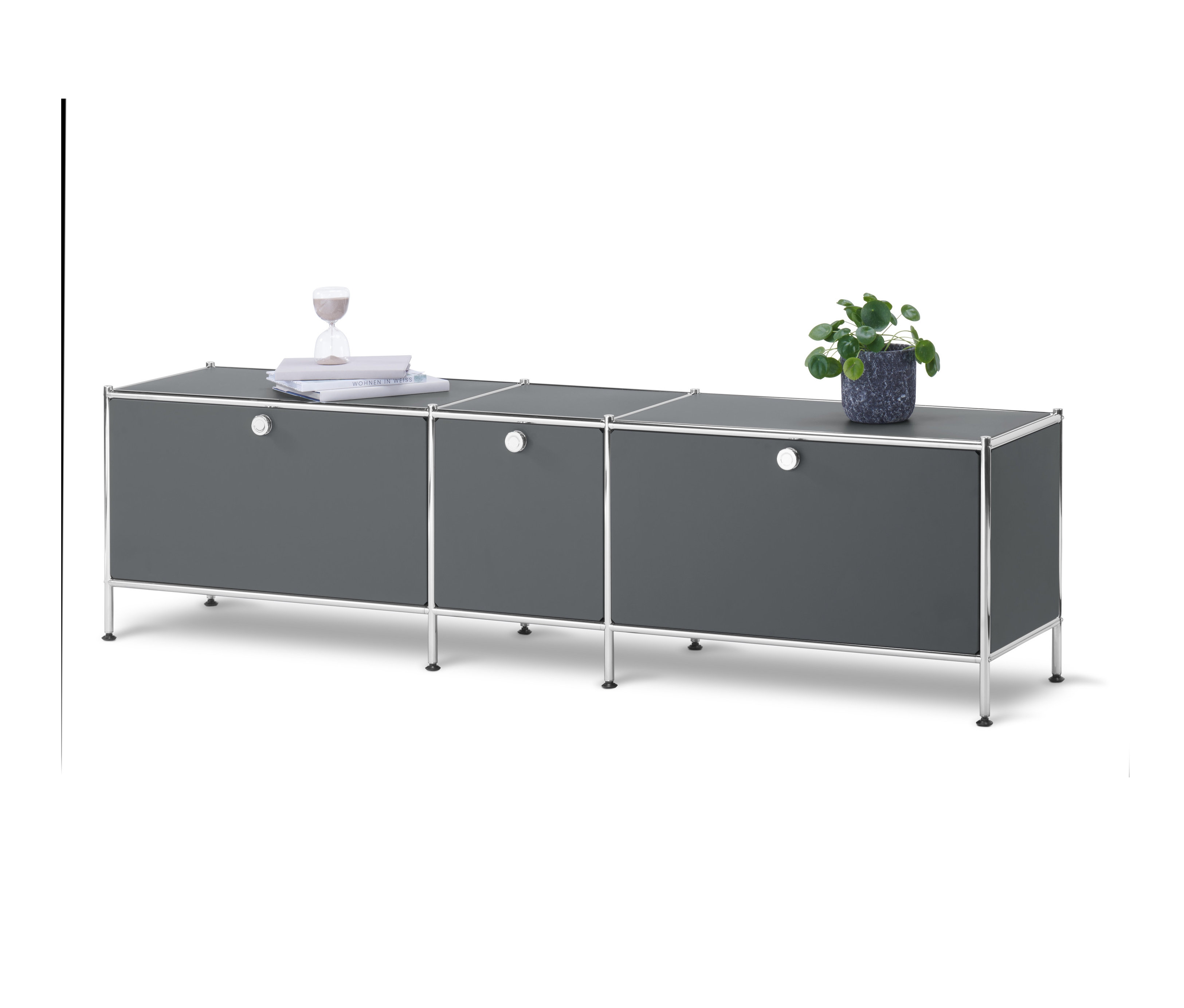 Ein graues Lowboard »CN3« mit 3 Klappen steht vor einem weißen Hintergrund. Auf dem Lowboard stehen eine Topfpflanze, Bücher und eine Sanduhr.