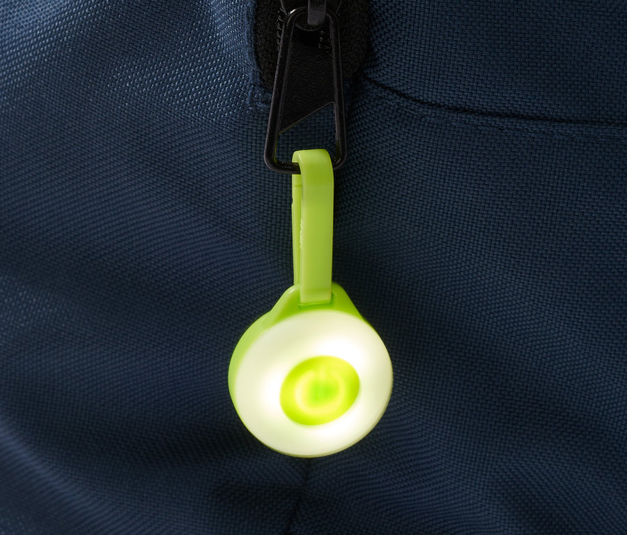 Ein grüner 3 LED-Anhänger hängt an einem Reißverschluss einer blauen Tasche.