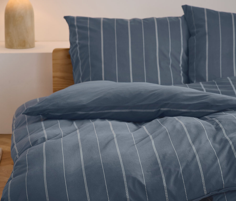 Winterjersey-Bettwäsche in Normal- und Übergröße mit blau-weißem Streifenmuster auf einem Bett.