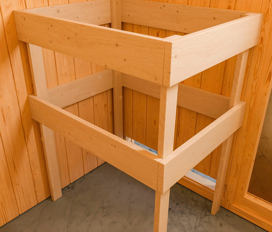Unfertige Holzkonstruktion des Karibu Saunahauses "Gwen" steht auf einem grauen Boden an einer holzgetäfelten Wand.