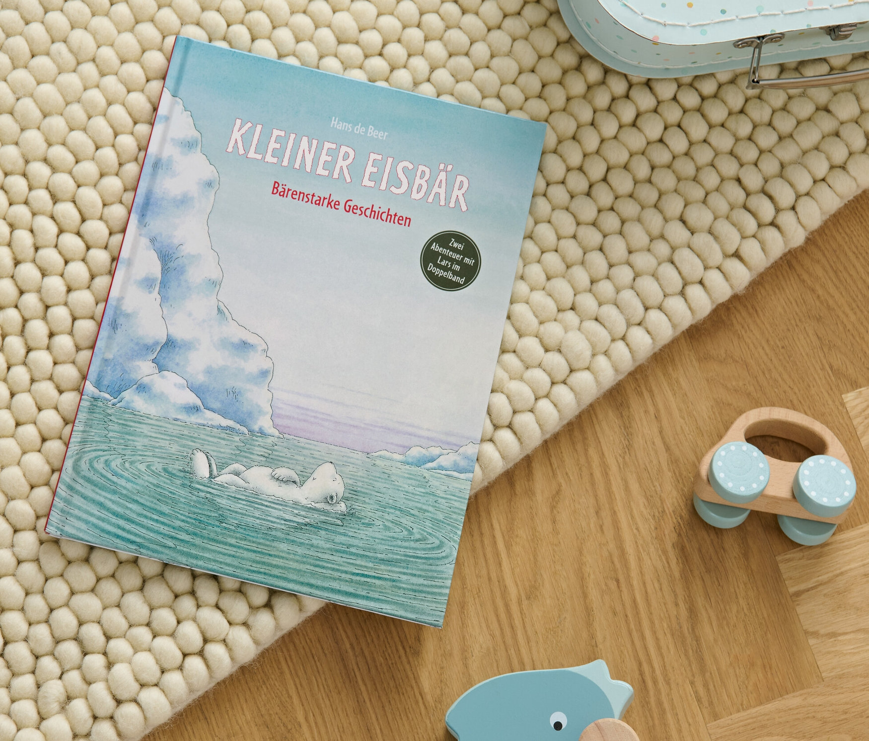 Das Buch "Kleiner Eisbär – bärenstarke Geschichten" liegt auf einem beige Teppich neben Holzspielzeug.