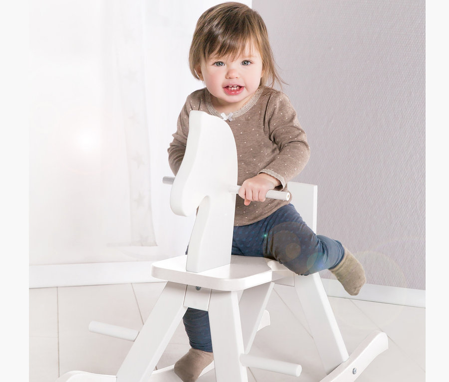 Ein Kind sitzt auf einem weißen Schaukelpferd von roba.