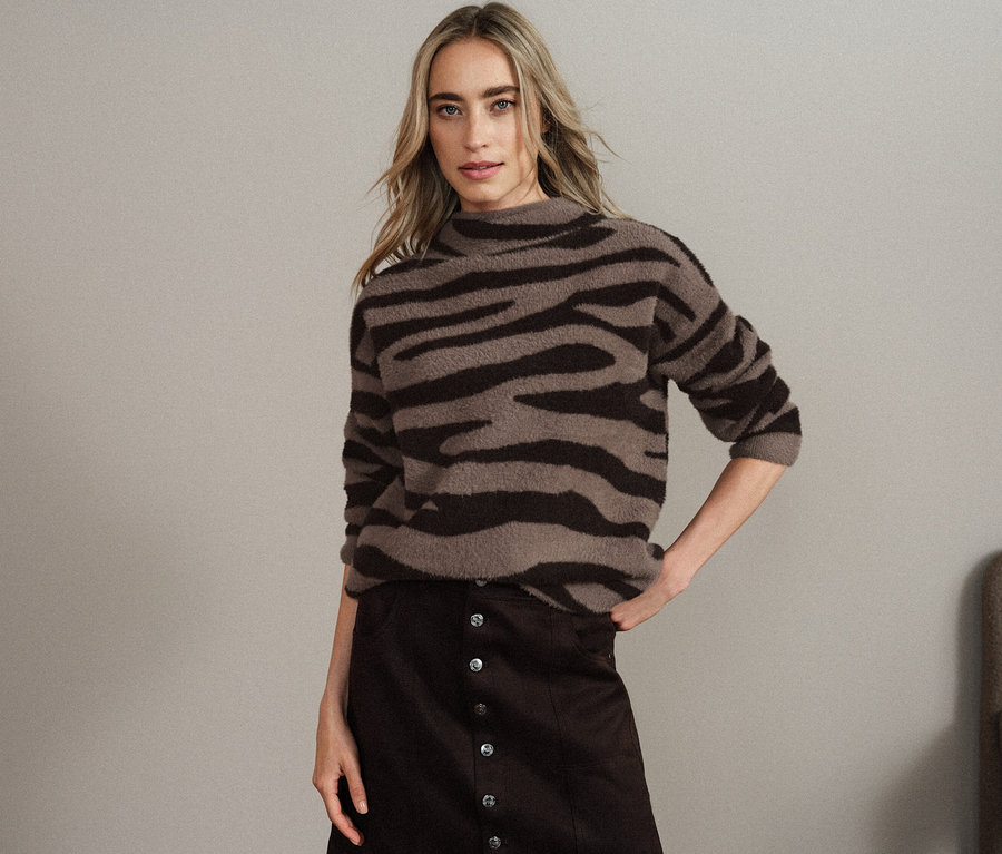 Frau posiert in braun-schwarzem Pullover mit Tiermuster und braunem Rock.