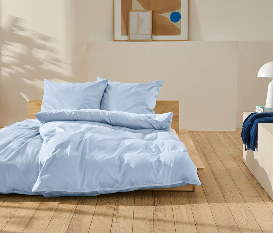 Hellblaue Bettwäsche auf einem Holzbett in einem Schlafzimmer.