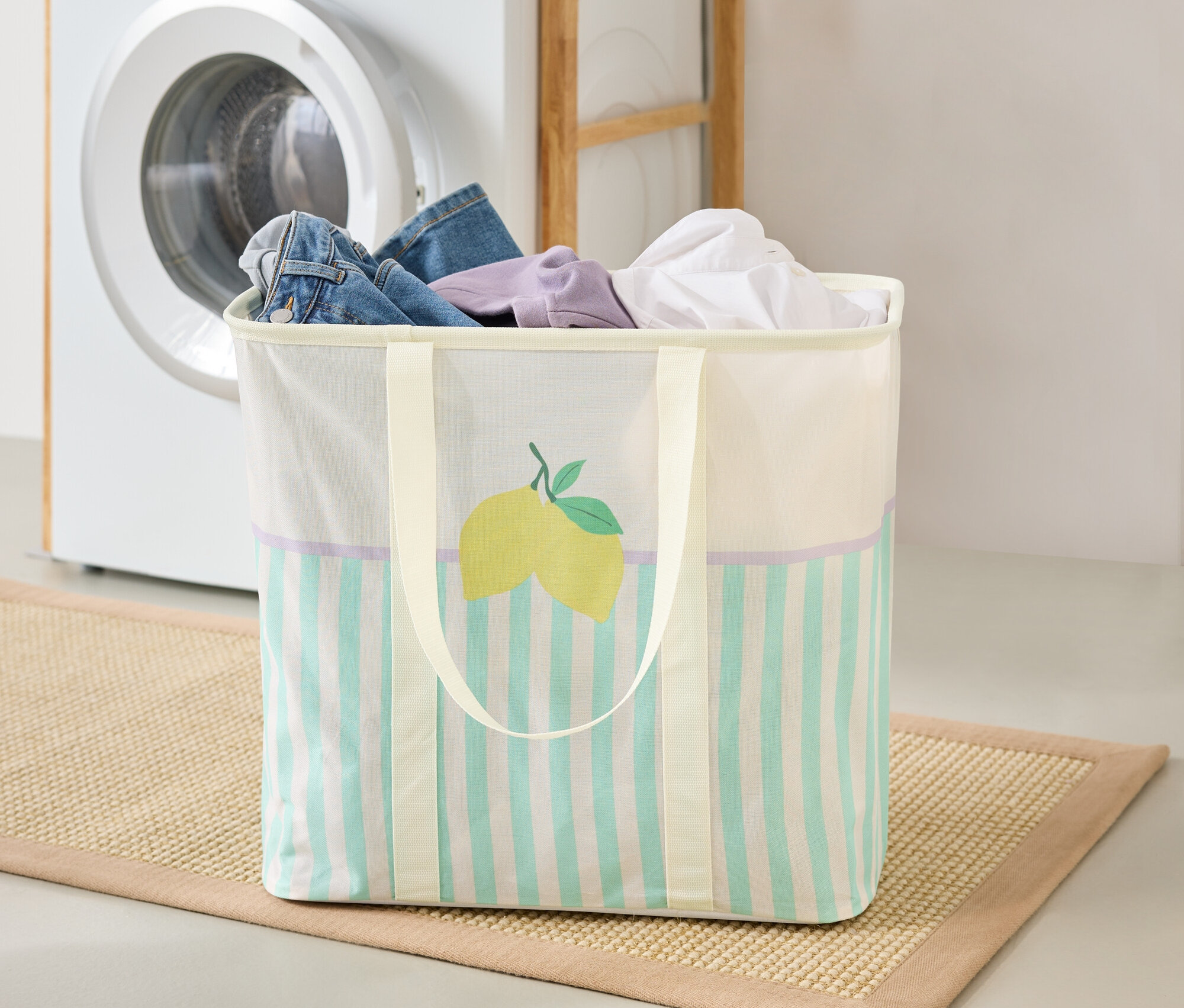 Ein Wäschekorb mit Zitronenmotiv steht auf einer Matte in einer Waschküche, im Hintergrund befinden sich eine Waschmaschine und ein Regal.