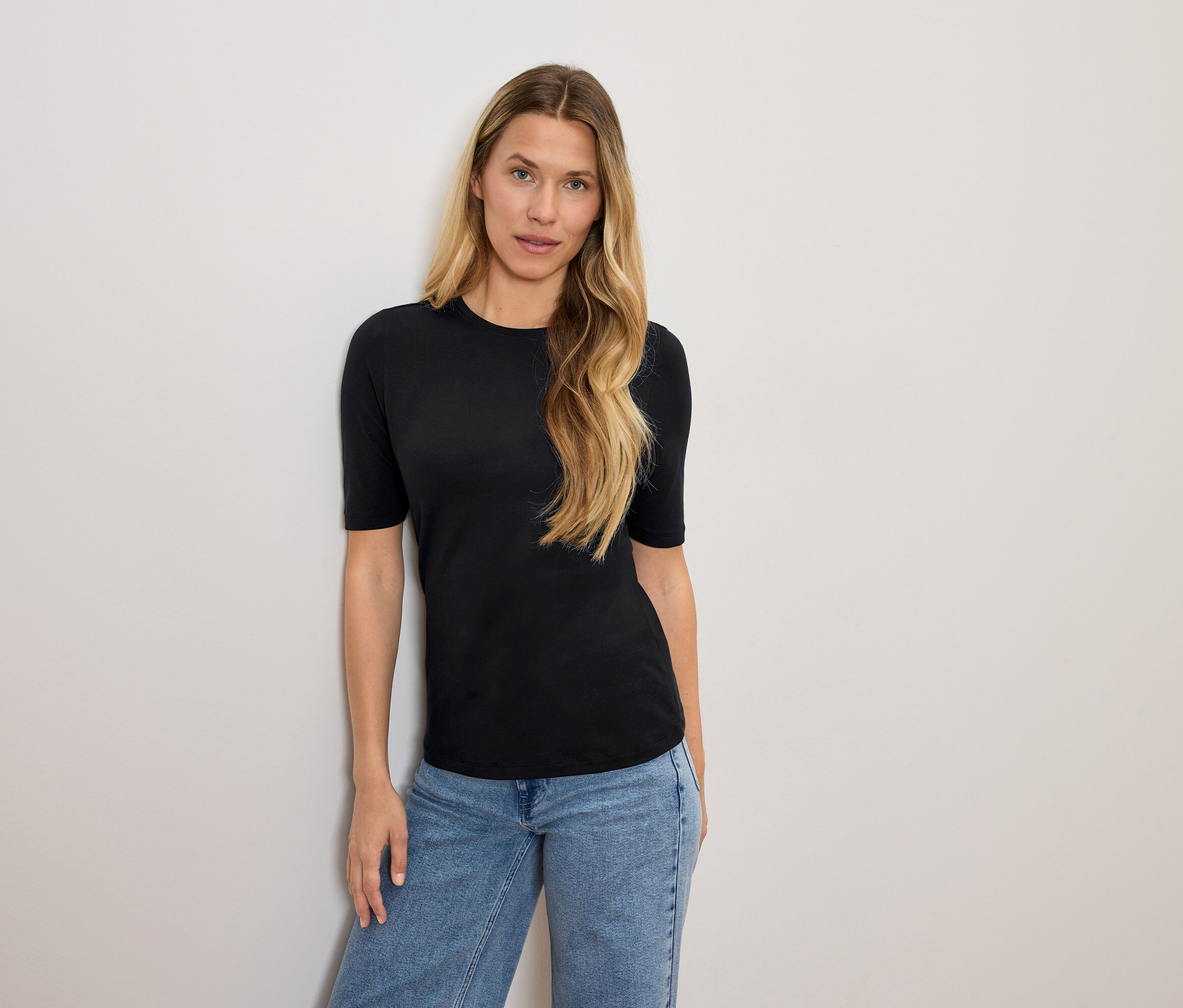 Frau mit blonden Haaren posiert in einem schwarzen T-Shirt und blauen Jeans.