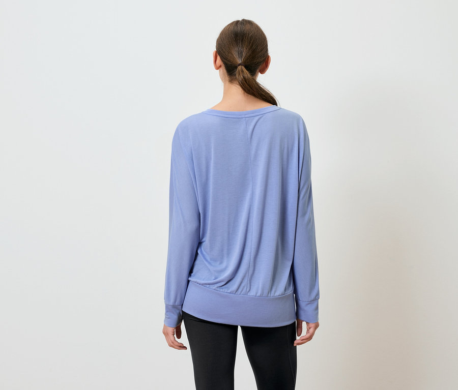 Frau mit dem Rücken zur Kamera trägt ein blaues Langarmshirt und eine schwarze Hose.