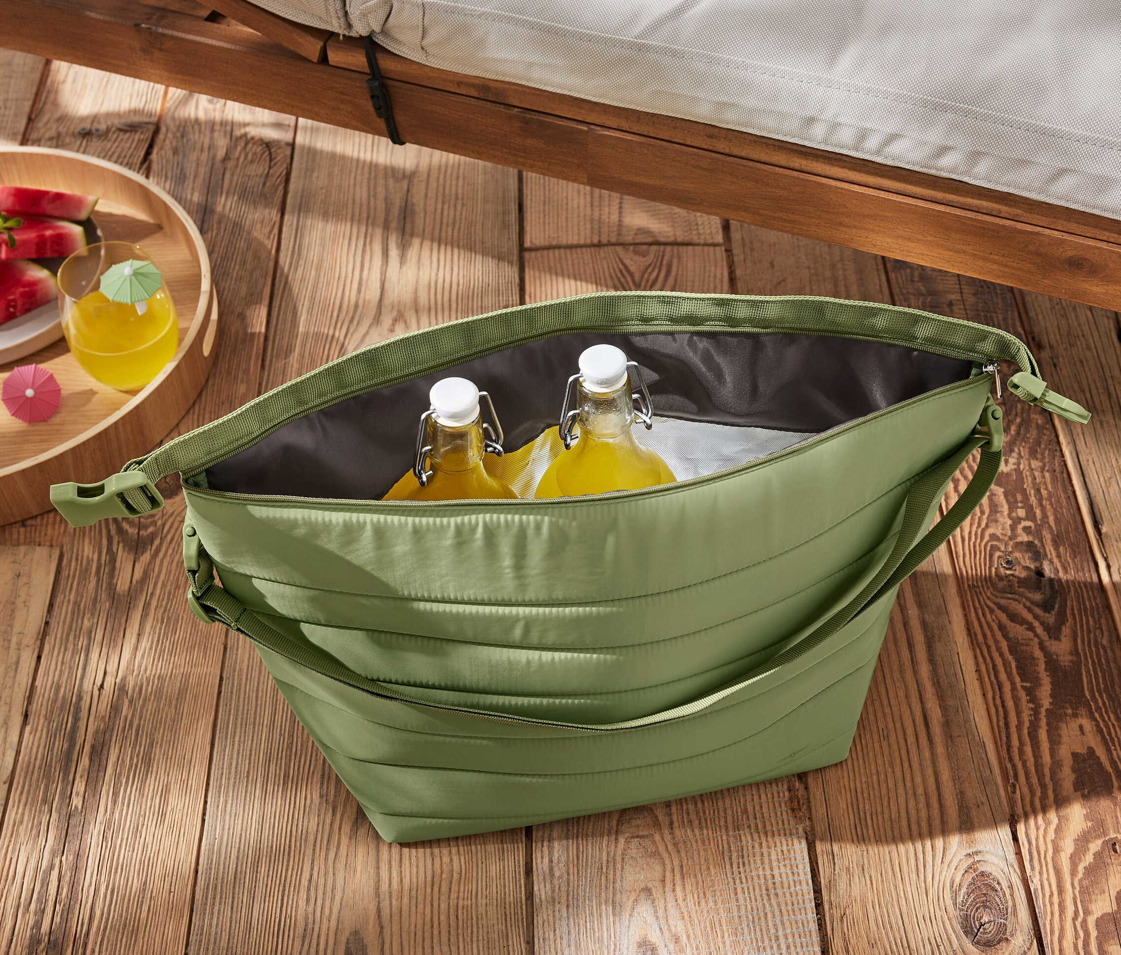 Eine grüne Kühltasche mit Flaschen und Wassermelone auf einem Holztisch.