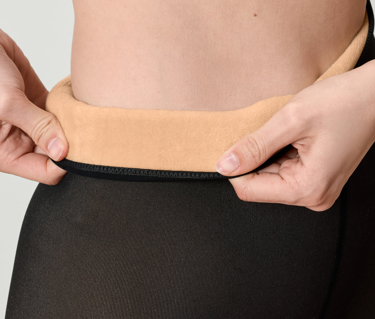 Detailaufnahme einer Frau, die den Bund einer schwarzen Strumpfhose mit beigem Fleecefutter hochzieht.