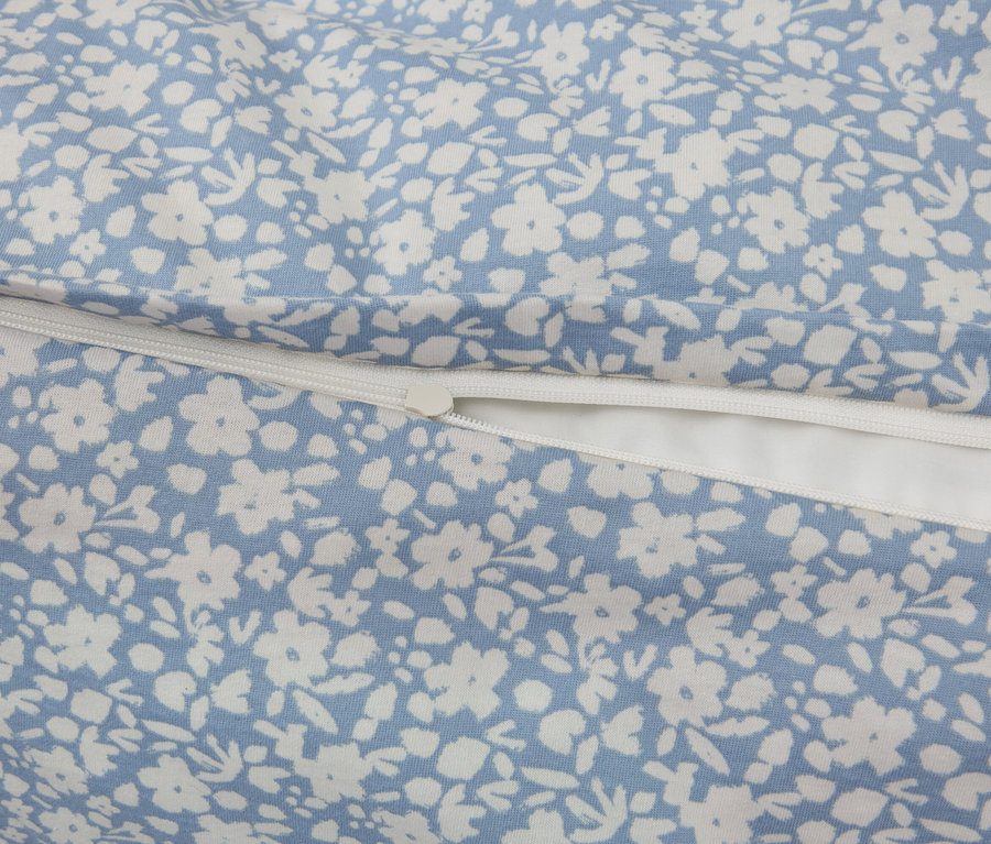 Detailaufnahme eines Stoffes mit blauem Hintergrund und weißem Blumenmuster, ergänzt durch einen weißen Reißverschluss.