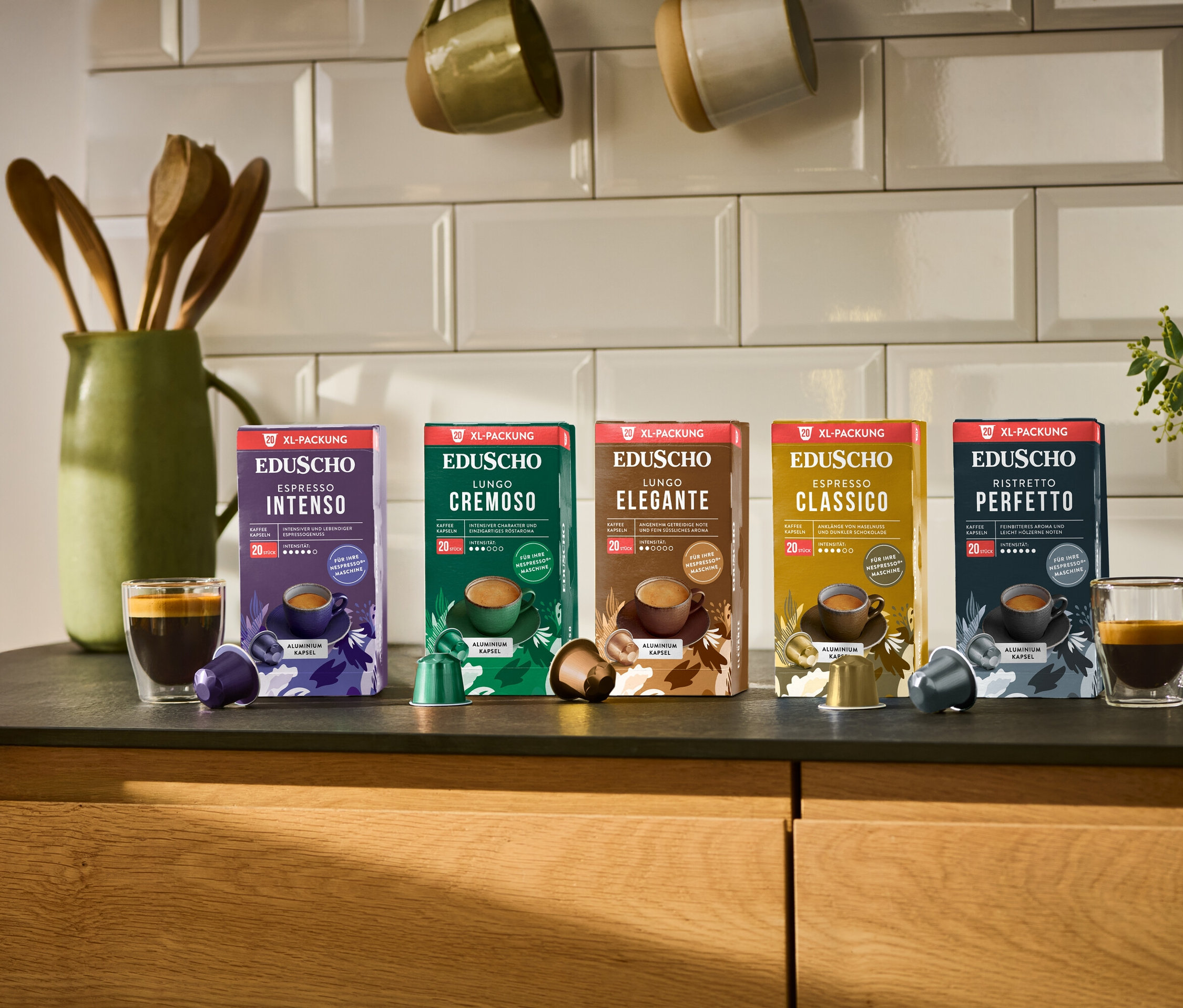 Fünf Packungen Eduscho Kaffeekapseln stehen auf einer Küchentheke, darunter Espresso Classico, Lungo Elegante, Lungo Cremoso, Ristretto Perfetto und Espresso Intenso.