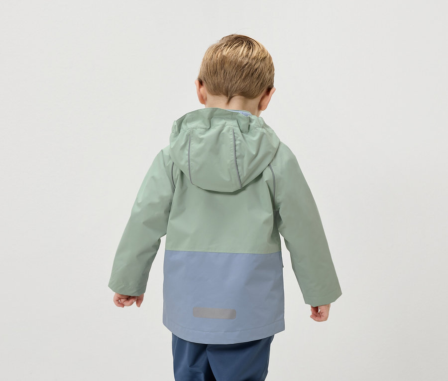 Rückansicht eines Kindes mit blonden Haaren, das eine zweifarbige Jacke in Grün und Blau trägt.