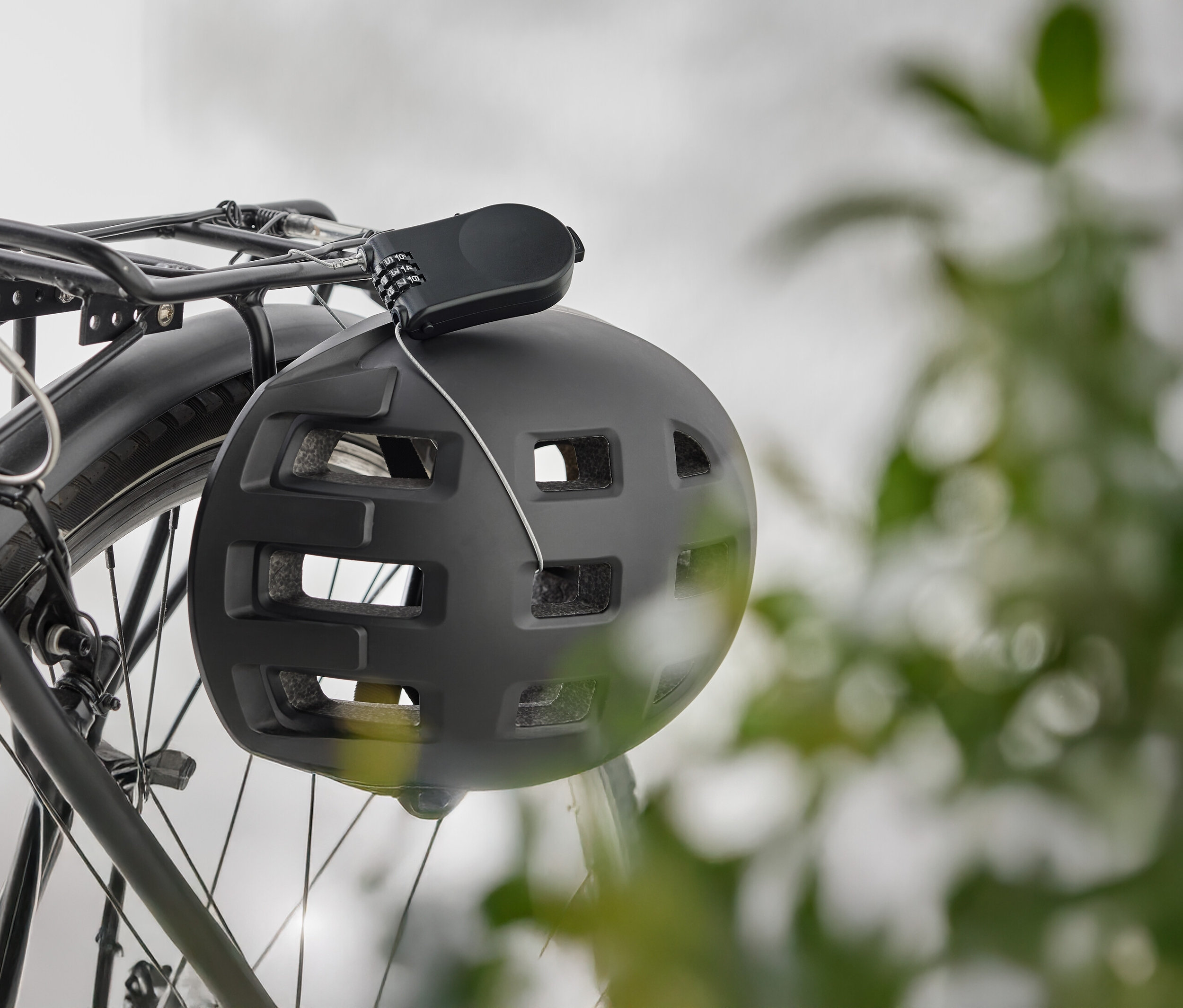 Ein schwarzer Fahrradhelm hängt mit einem Zahlenschloss an einem Fahrradgepäckträger.