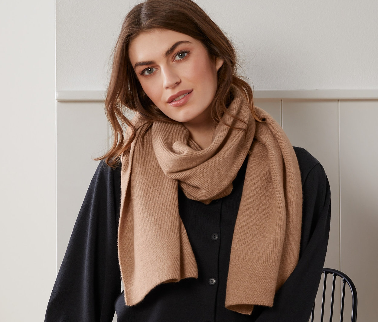 Frau sitzt und trägt einen beigen melierten Strickschal.