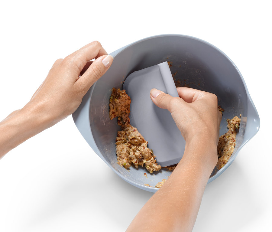 Zwei Hände verwenden einen grauen Teigschaber aus einem Profi-Backhelfer-Set, um Teig aus einer blaugrauen Schüssel zu kratzen.