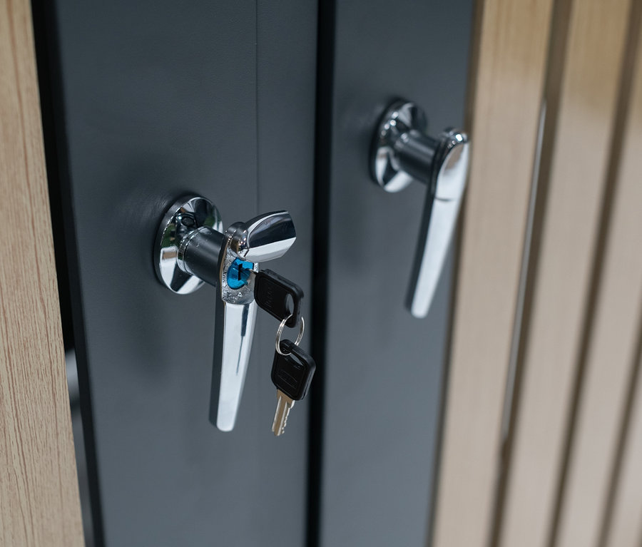 Detailaufnahme von zwei grauen Türen des 'Mülltonnenbox mit Blumenkasten, 2er' mit Chromgriffen, wobei ein Schlüssel in einem Schloss steckt.