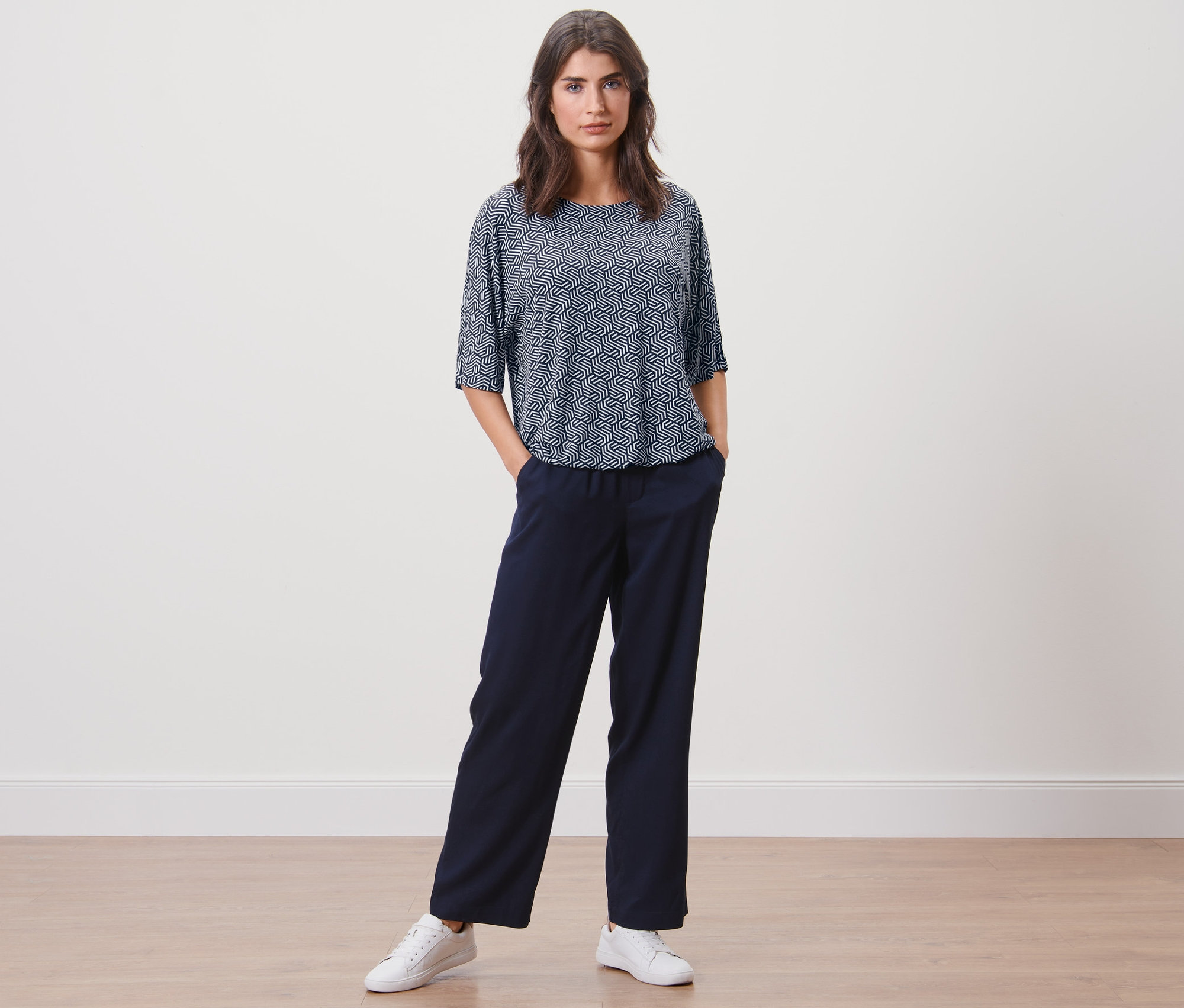 Frau posiert in blauem bedruckten Blusenshirt und marineblauer Hose.