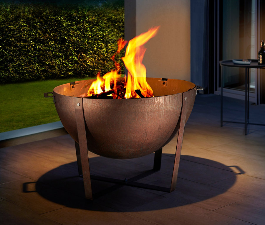 Feuer brennt in Buschbeck Plancha-Grill »Dakota«. Im Hintergrund sind Grünflächen und Möbel zu sehen.