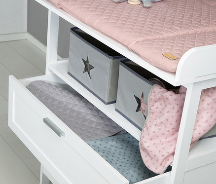 Weißes roba Kinderzimmer-Set mit Bett und Kommode, oben eine rosa Decke und ein Teddybär, darunter zwei graue Kisten und eine offene Schublade mit Textilien.