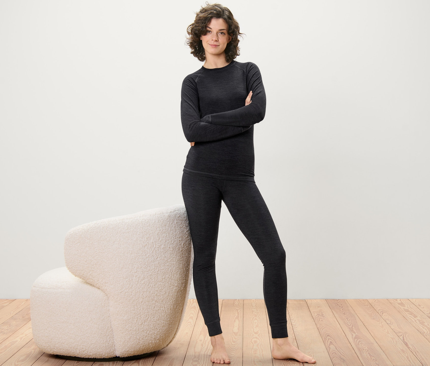 Frau posiert in langer Unterhose mit RWS-zertifizierter Wolle und Oberteil auf Holzboden neben einem cremefarbenen Sessel.