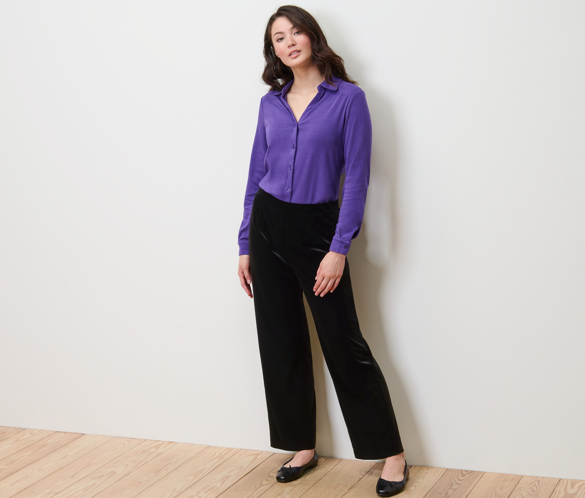 Frau posiert in lila Hemd und Samt-Palazzohose.