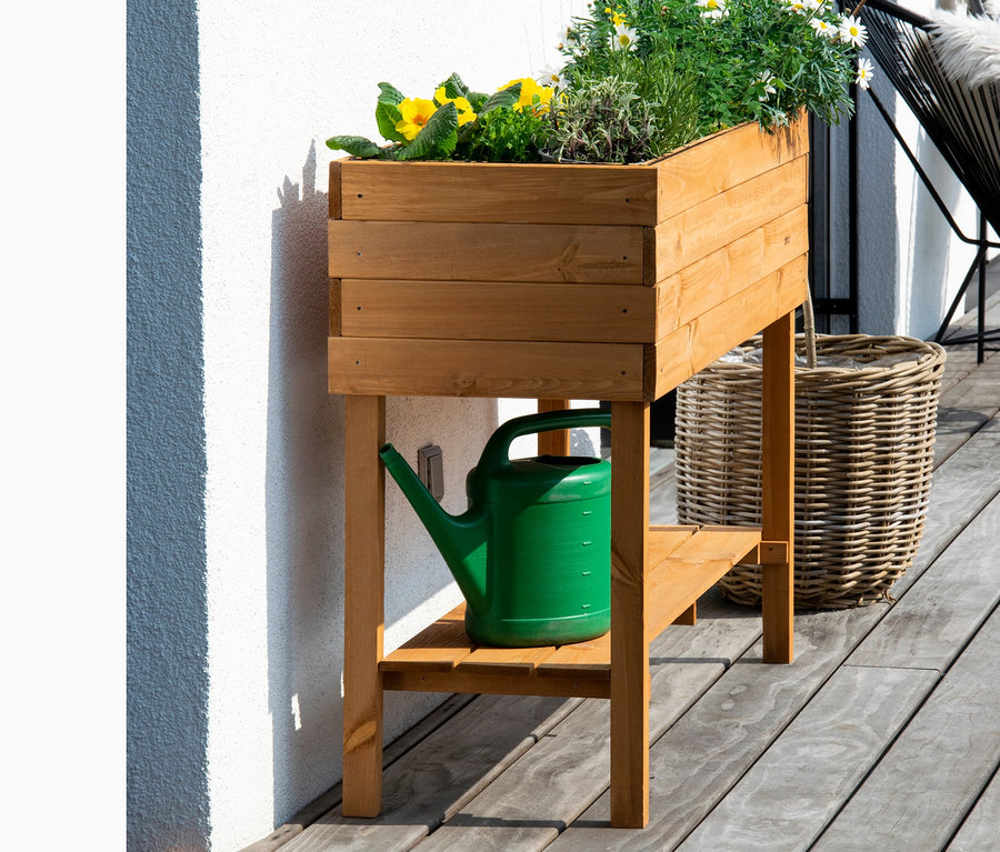 Ein hölzernes Hochbeet, ca. 117 x 80 x 40 cm, bepflanzt mit Blumen, darunter eine grüne Gießkanne.