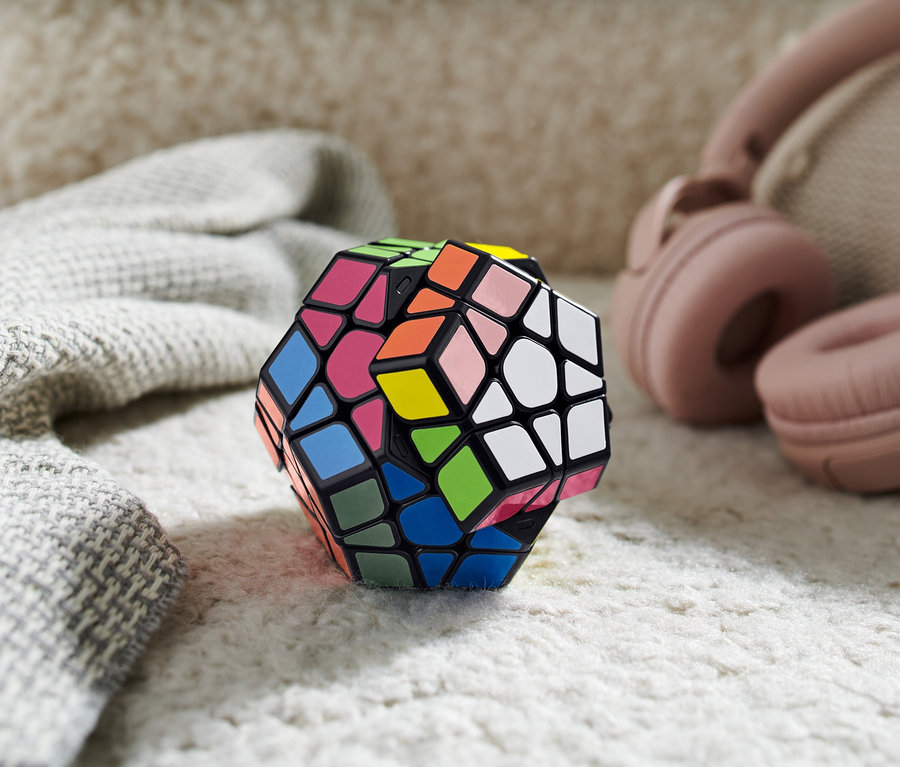 Ein bunter IQ-Würfel »Polygon« liegt auf einem zotteligen Teppich neben Kopfhörern und einem Schal.