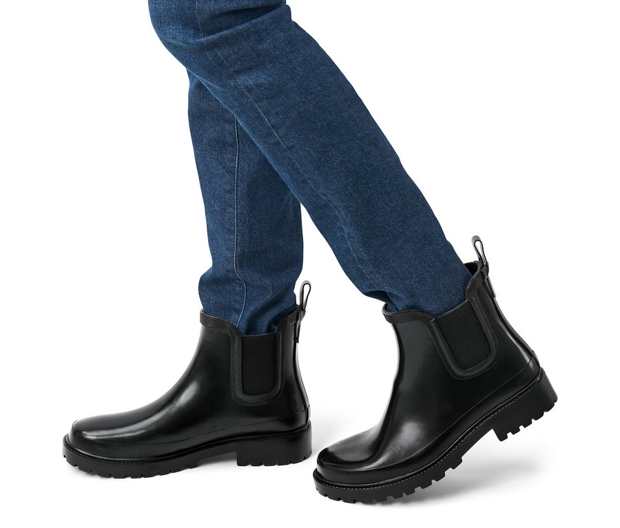 Beine einer Person in Jeans und Regenstiefeletten.