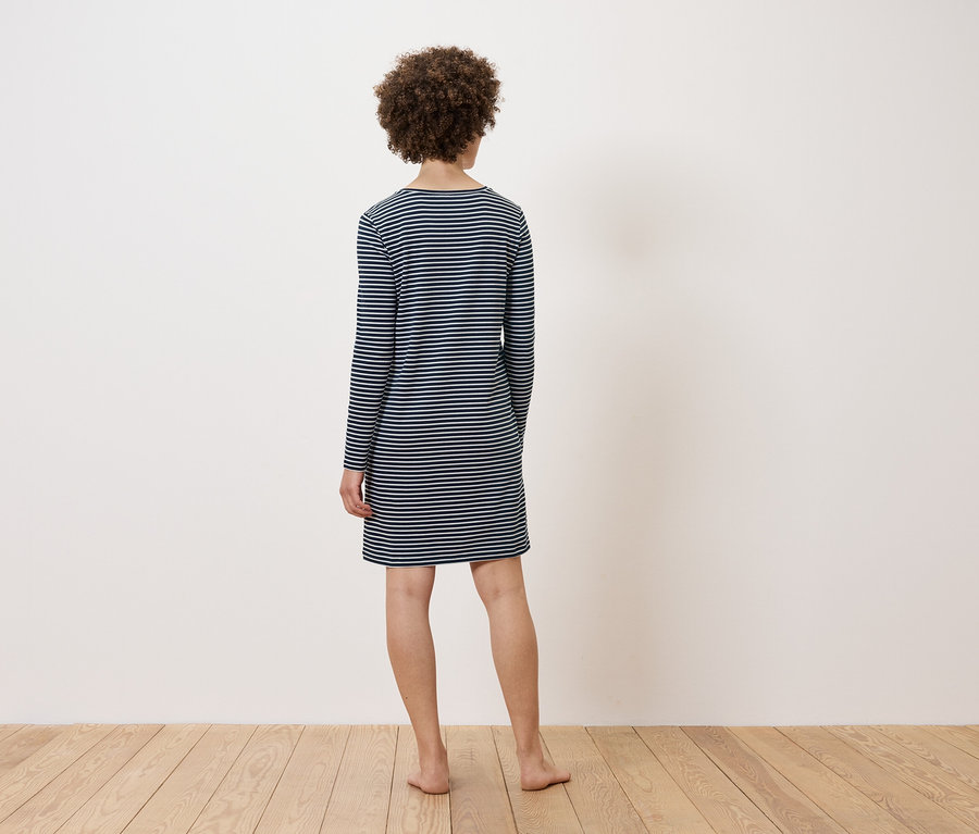 Frau steht mit dem Rücken zur Kamera und trägt ein gestreiftes Kleid.