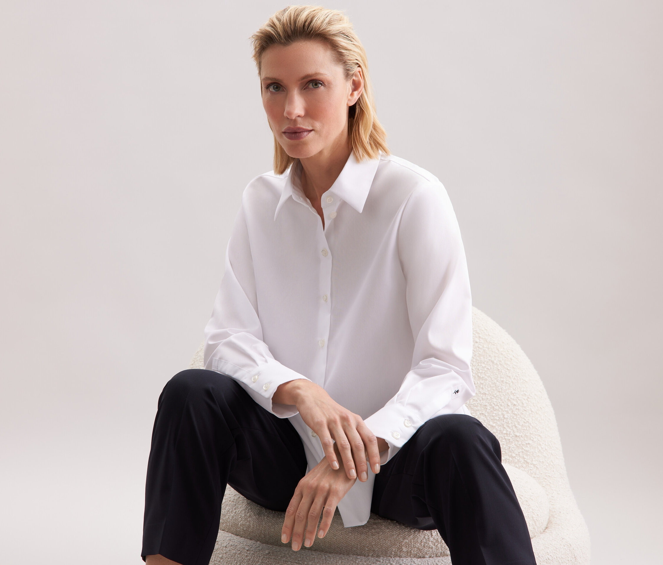 Frau sitzt auf einem Stuhl und trägt ein weißes Hemd und eine schwarze Hose.