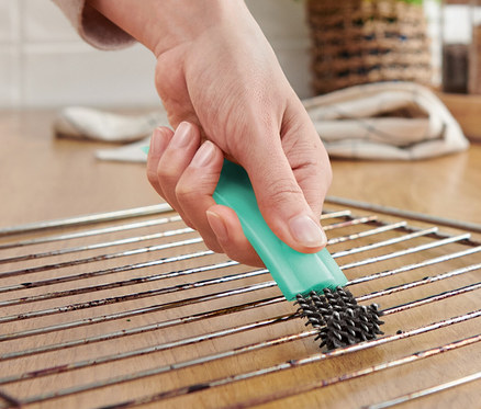 Person reinigt einen Ofenrost mit einer Backofenbürste mit Schaber.